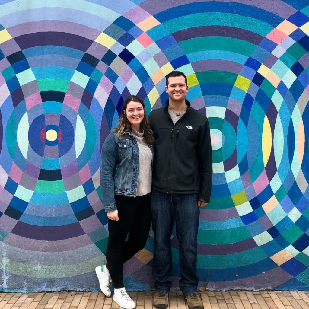 Woman and man standing in front of a blue and purple graphic mural.