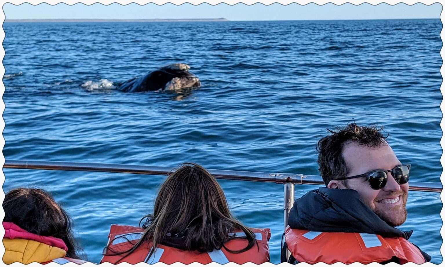 Three people on a boat looking at a whale surfacing