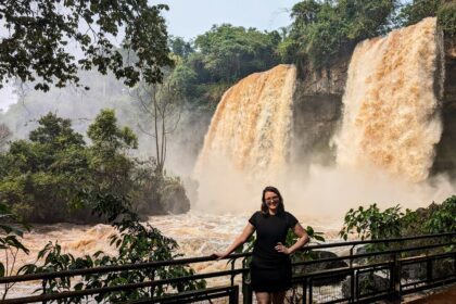 A woman standing in front of two orange waterfalls in a jungle - Iguazu Falls itinerary