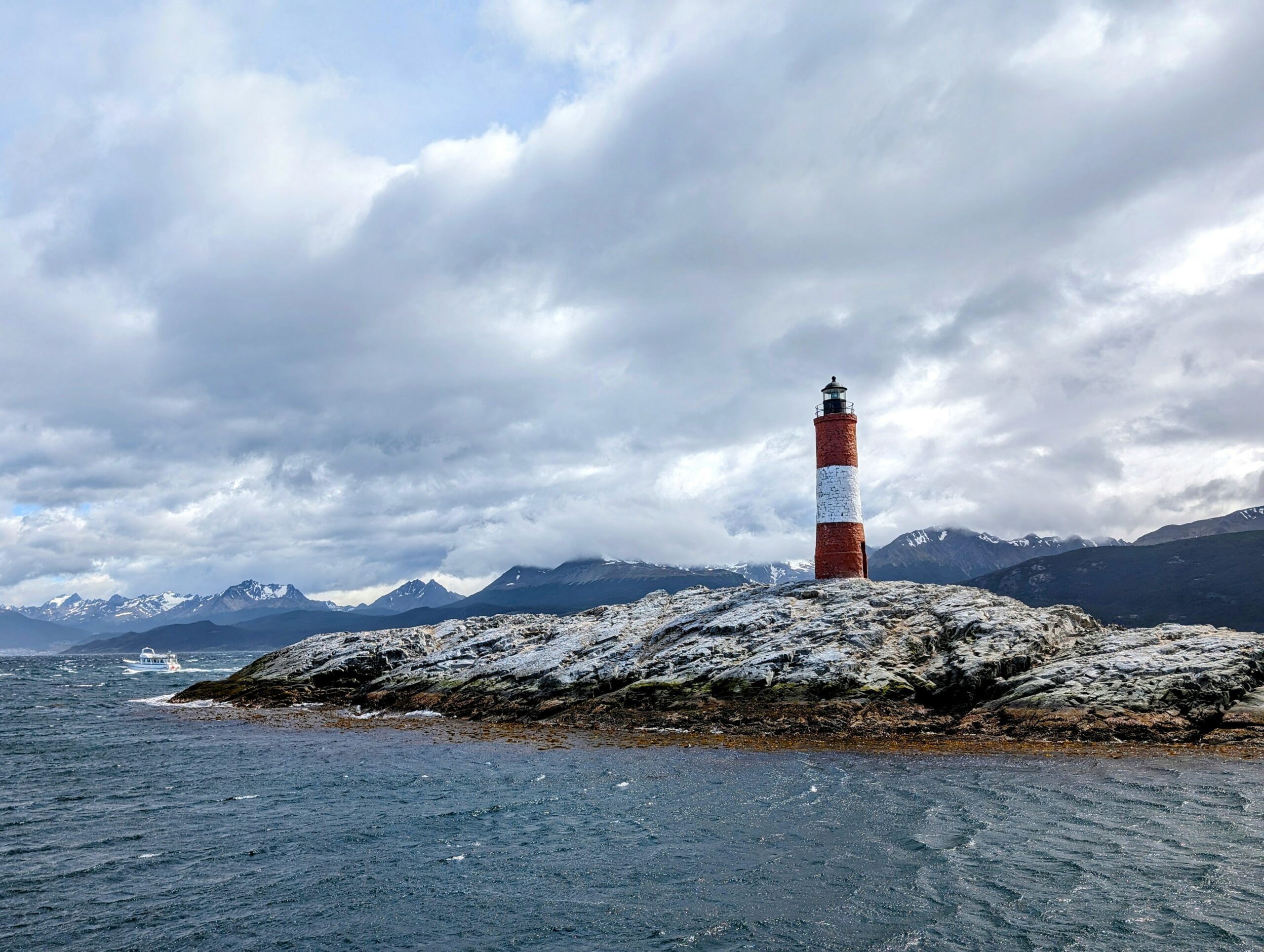A red and white lighthouse on a large rock island surrounded by a body of water - Best Things to Do in Ushuaia