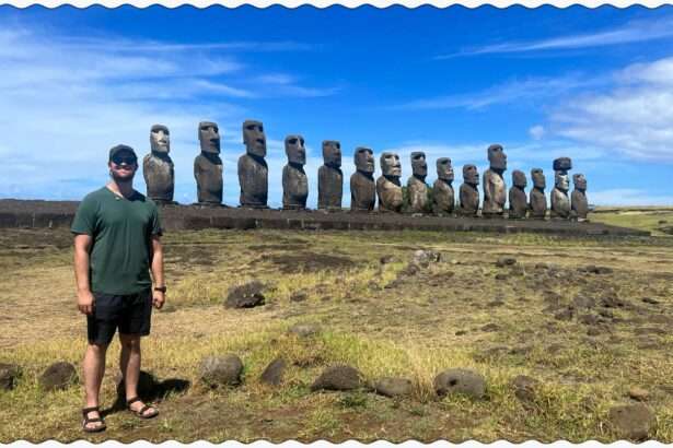 A man standing in front of a line of Easter Island heads behind a grassy field