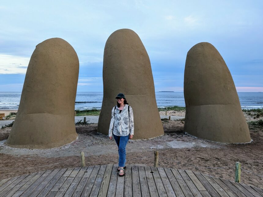 A woman standing in front of a large sculpture of someone's hands coming out of the ground - Things to do in Punta del Este