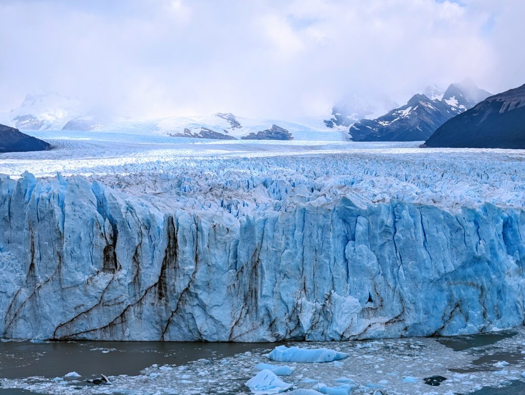 The facade of a glacier with broke icebergs and pieces floating in the water