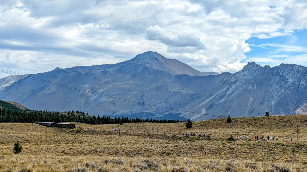 Large mountain with plains in front with a train riding through the landscape