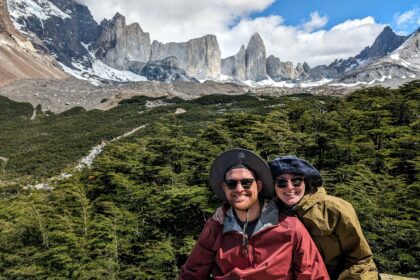 Two people sitting in front of mountains that are covered in snow - Torres del Paine W Trek - traveling to Patagonia