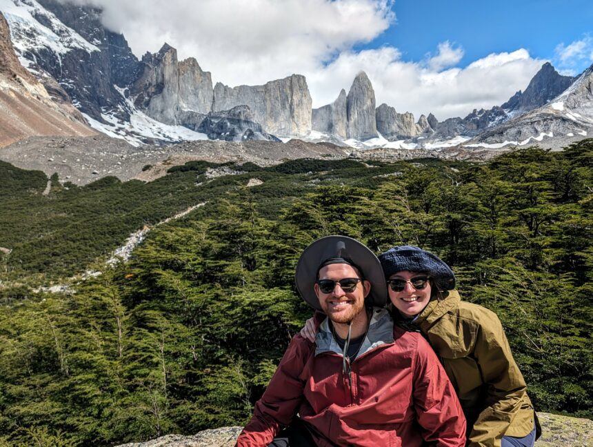 Two people sitting in front of mountains that are covered in snow - Torres del Paine W Trek - traveling to Patagonia