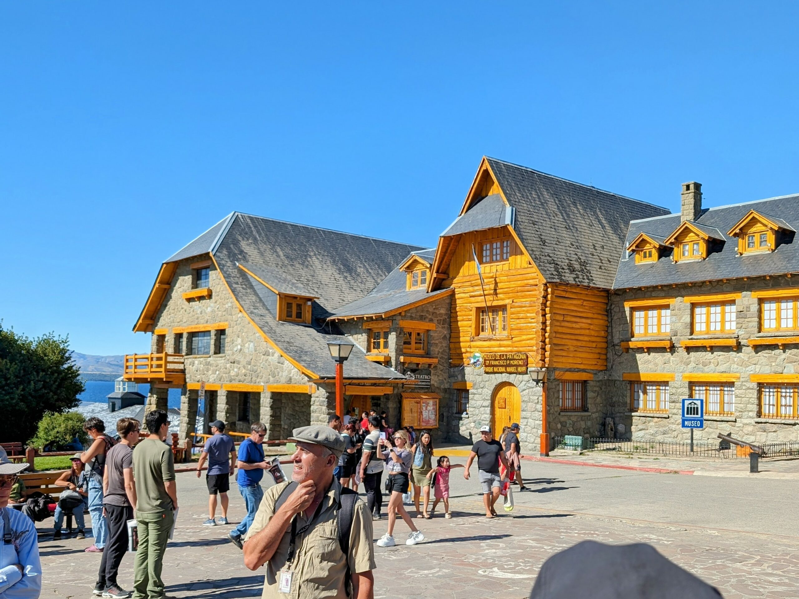 A tour guide standing in a town square with wood-log buildings around it - what to do in bariloche