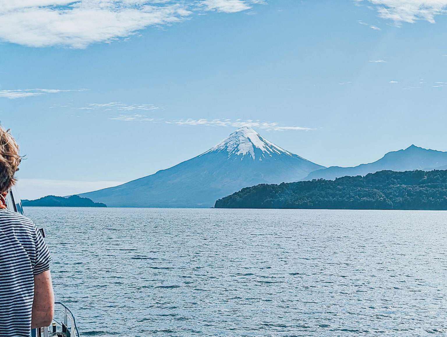A person on a boat on a lake in front of volcanos and mountains - Cruce Andino