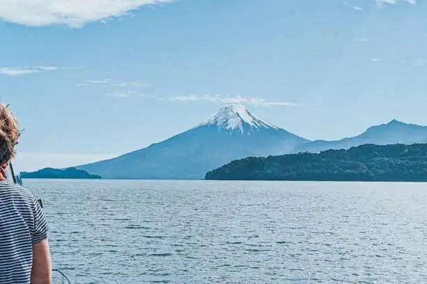A person on a boat on a lake in front of volcanos and mountains - Cruce Andino