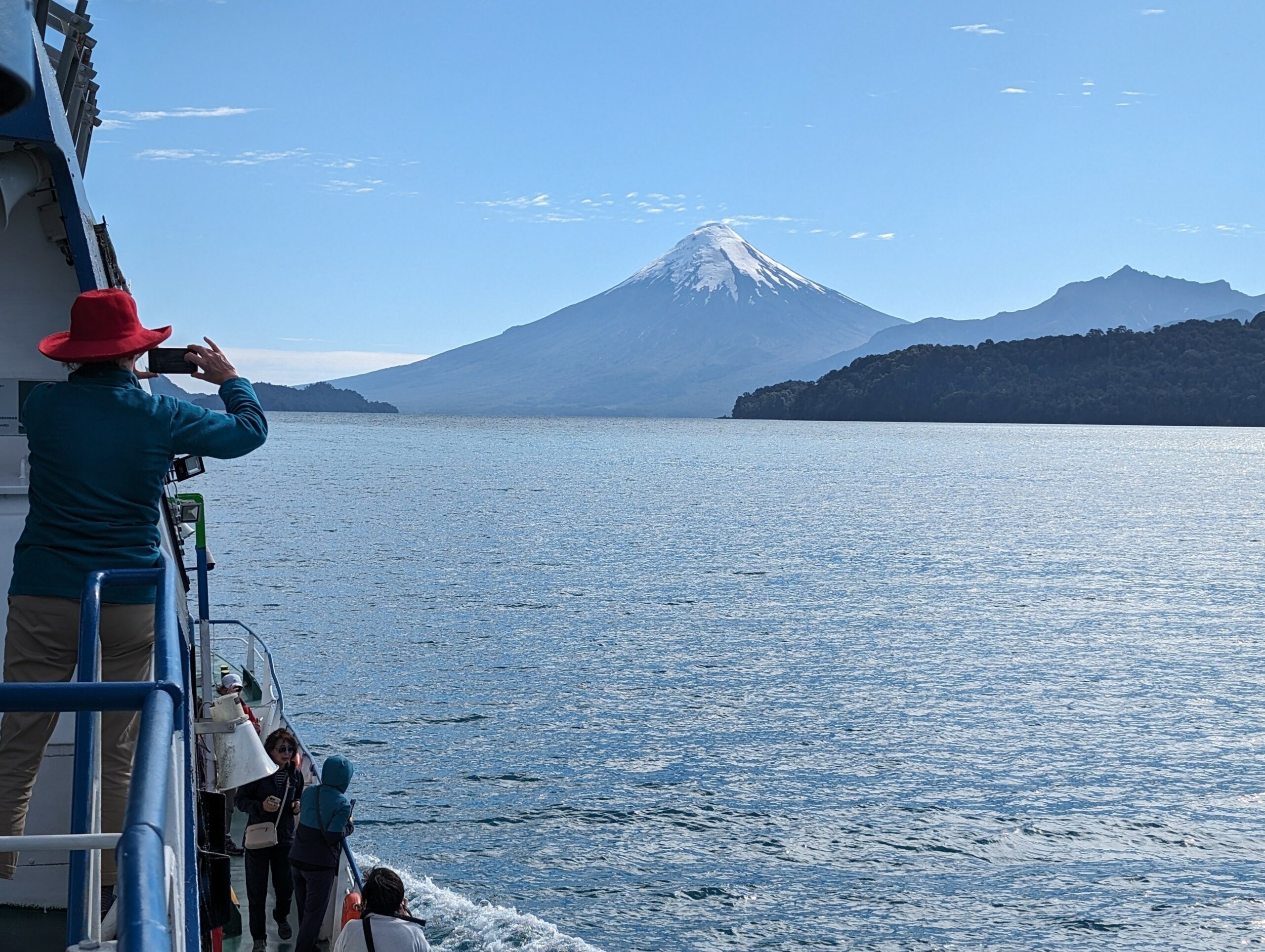 A woman with a red hat taking a photo of a volcano from a boat