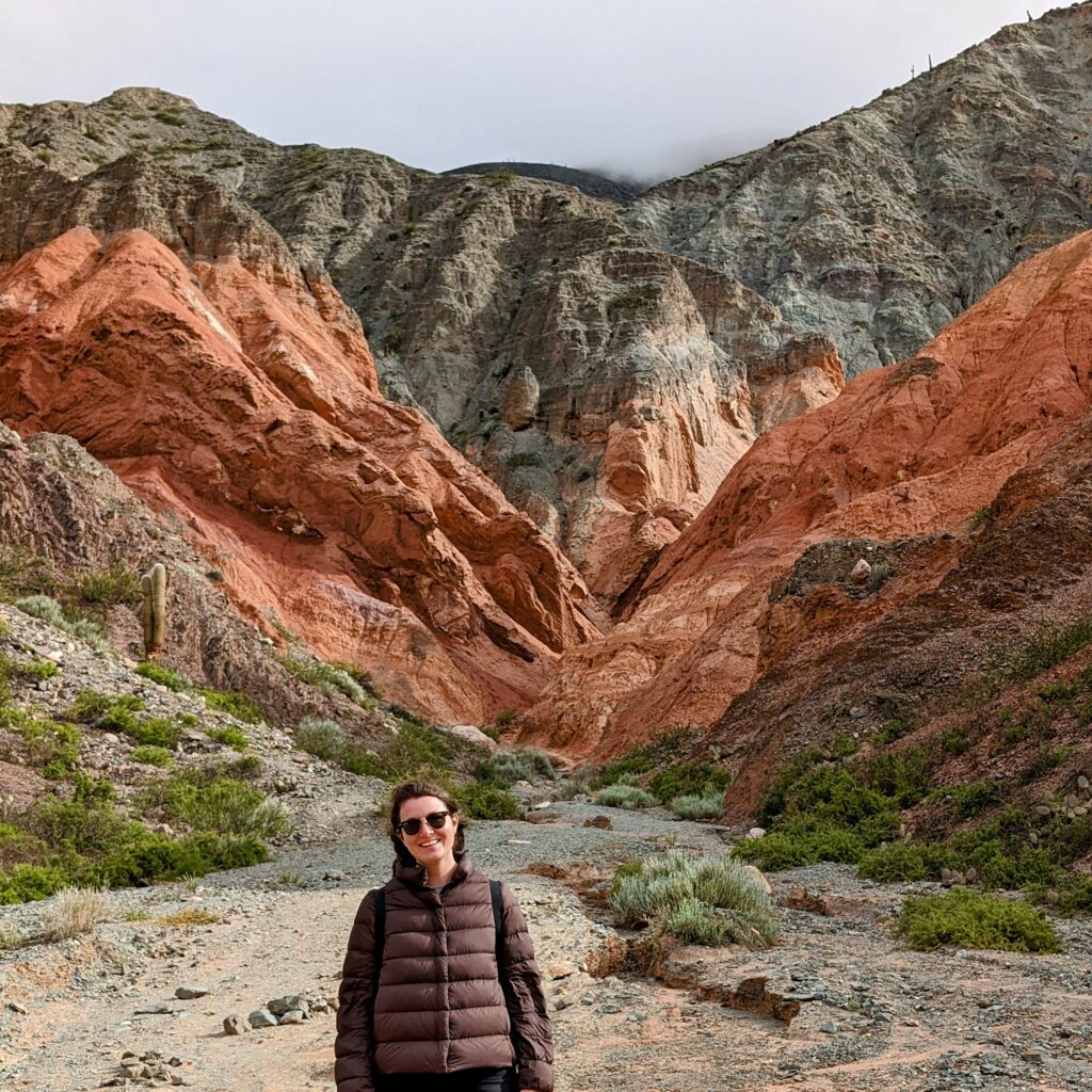 A person standing in front of a red and brown mountain that can be seen when visiting Salta