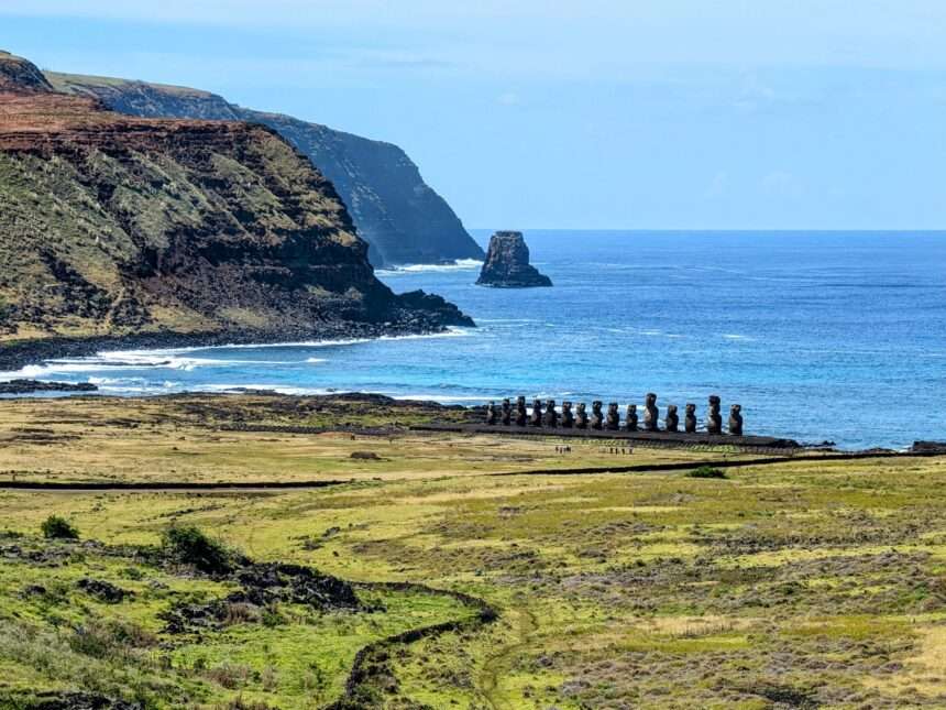 The view overlooking a grassy area leading to the ocean with some statues on the edge of the land - How to visit Easter Island