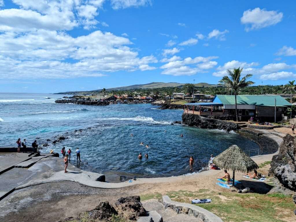 People hanging out in and around a swimming hole along the coast of a town - how to visit easter island