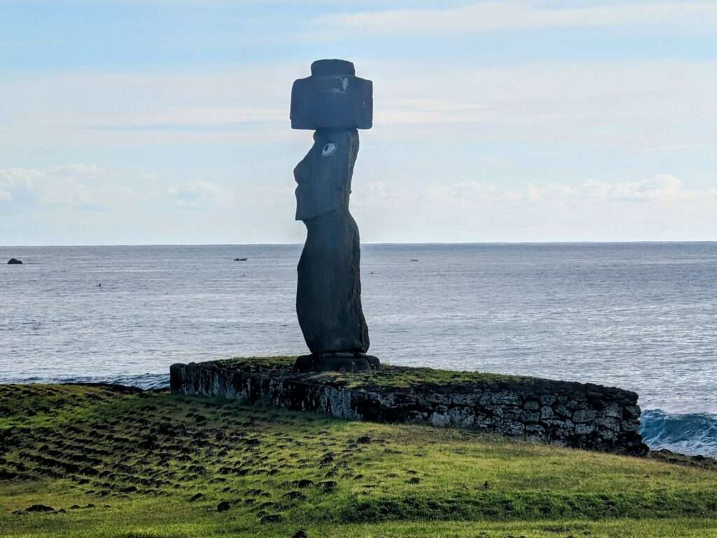 A stone statue on a platform with the ocean behind - How to Visit Easter Island