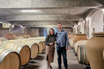 Two people standing in the middle of a wine barrel room with concrete ceiling - Best Mendoza Wineries
