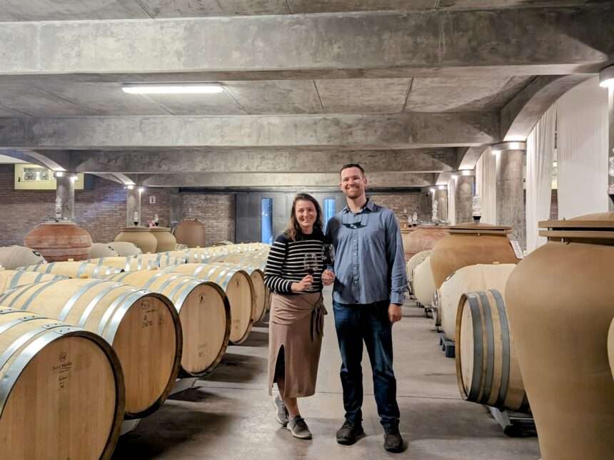 Two people standing in the middle of a wine barrel room with concrete ceiling - Best Mendoza Wineries