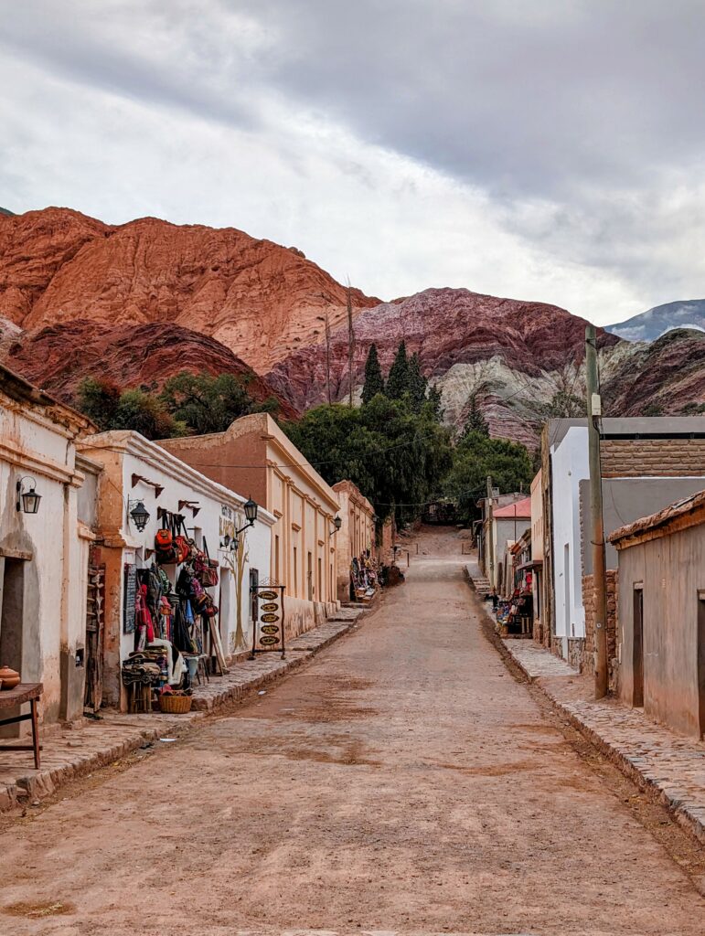 A red dirt street lined with adobe shops leading to a red mountain that can be seen when visiting Salta