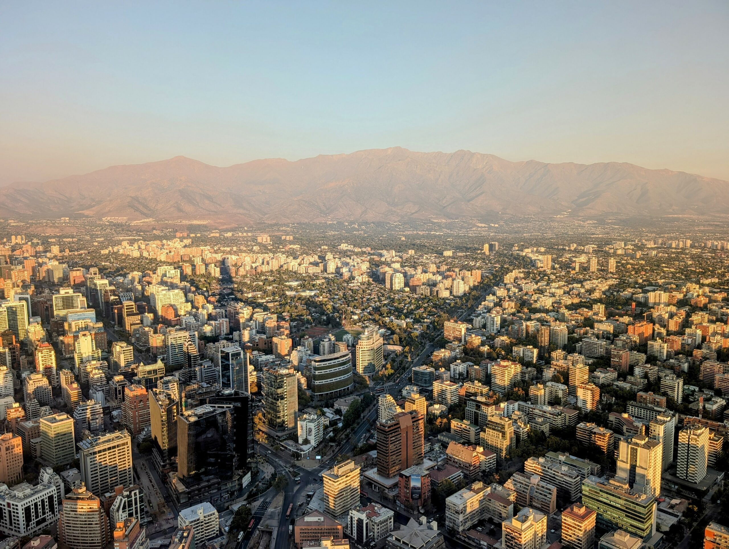 The view from the top of a skyscraper overlooking a city that's surrounded by mountains