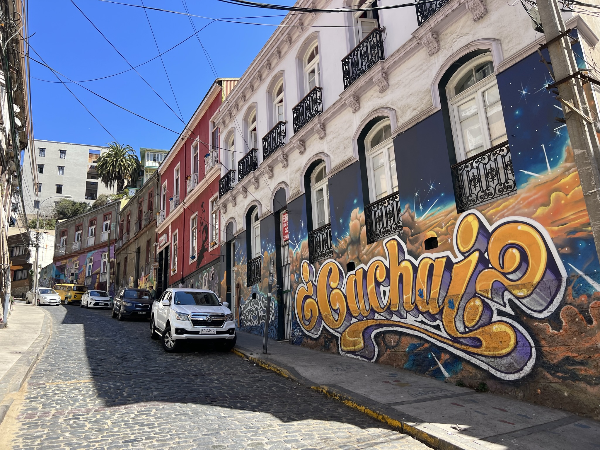 A cobblestone street going up a hill with murals on the buildings - Things to do in Santiago