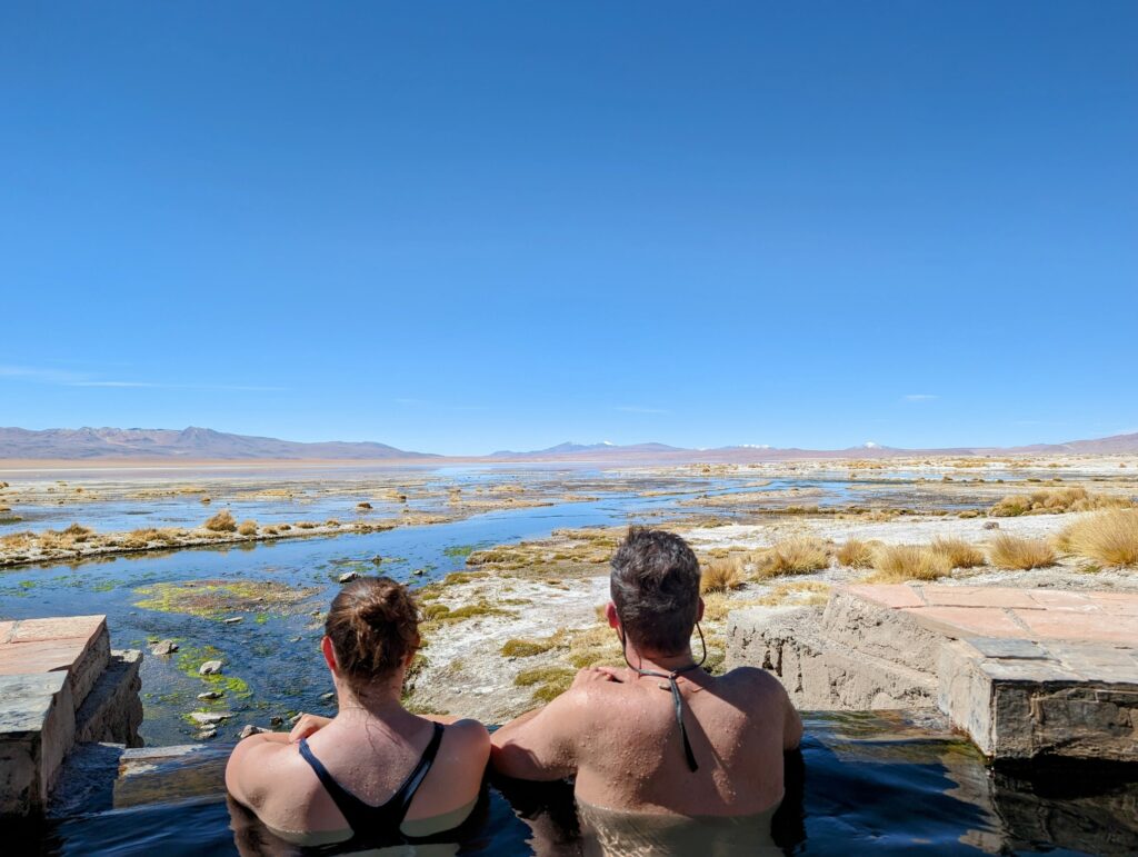 Two people sitting in a thermal bath looking over a wetland landscape on the Uyuni Salt Flats tour