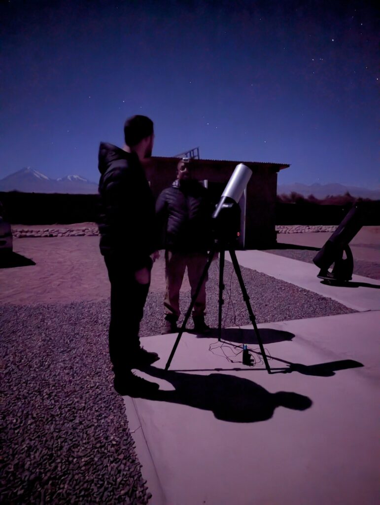 Two people standing around a telescope looking at the stars outside of San Pedro de Atacama