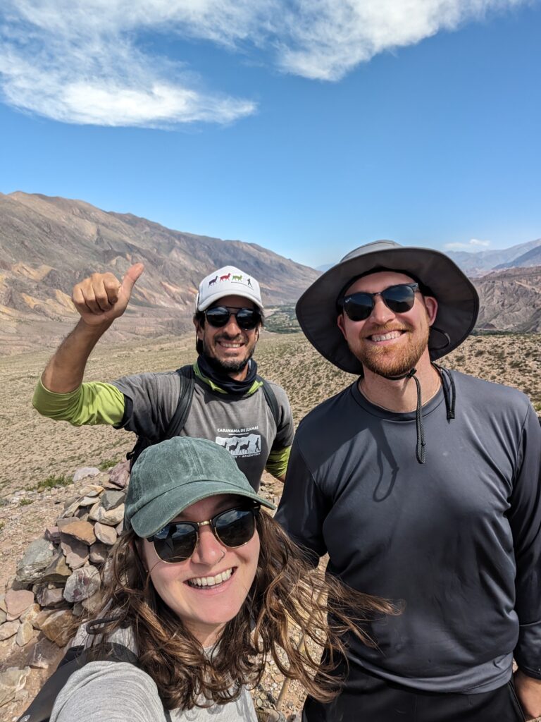 Three people smiling to a camera with a mountain in the background