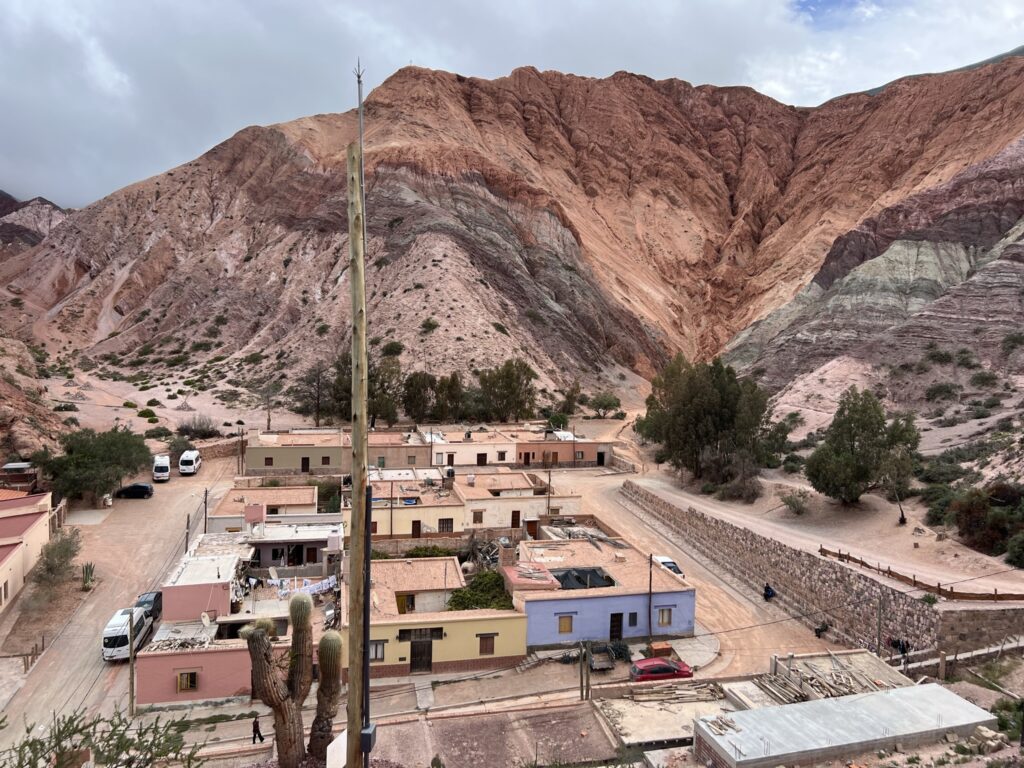 A few colorful buildings in front of a red and brown mountain