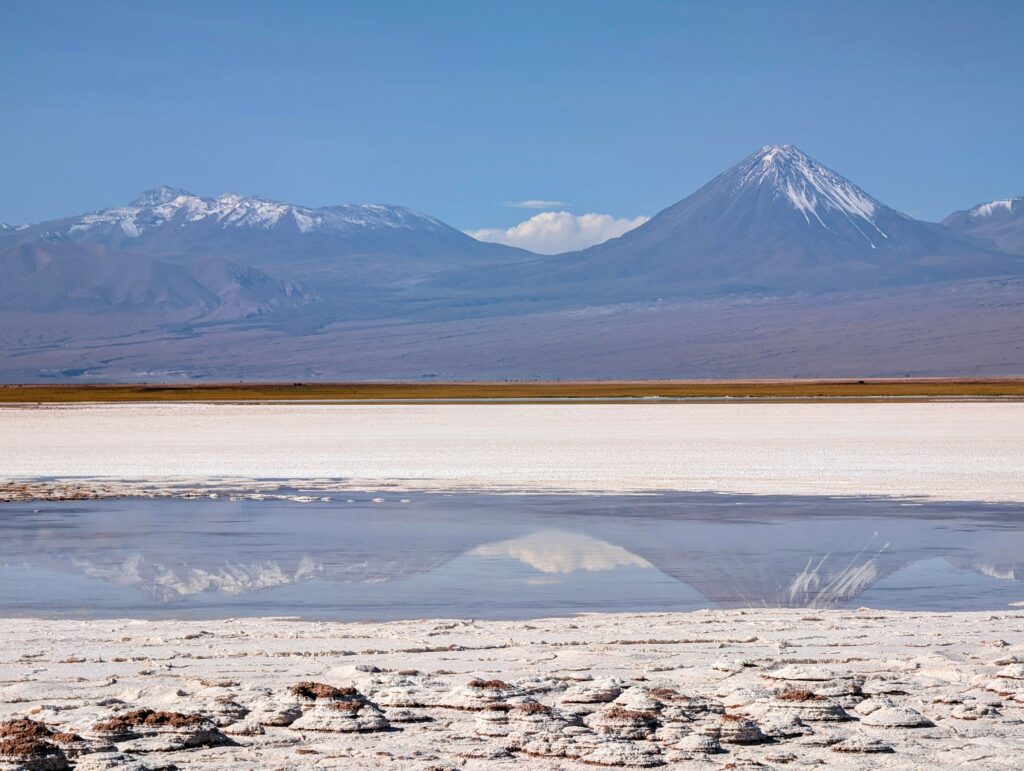 A blue lagoon surrounded by salt reflecting the mountains in the background outside of San Pedro de Atacama