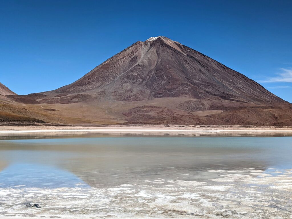 A blue-green lagoon with the reflection of a volcano on the Uyuni Salt Flats tour