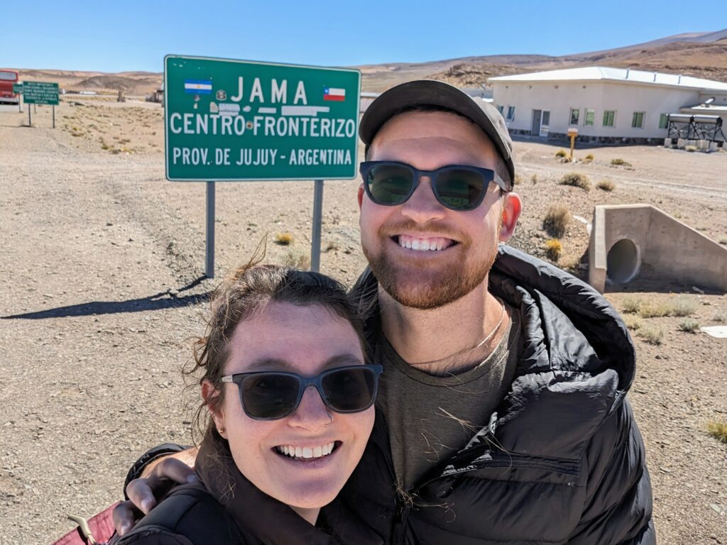 Two people in front of a mountain pass to cross the border between Chile and Argentina