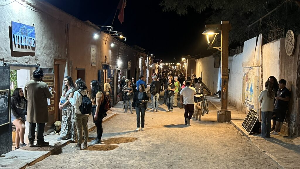 A pedestrian dirt street filled with people and lined with white clay retail buildings