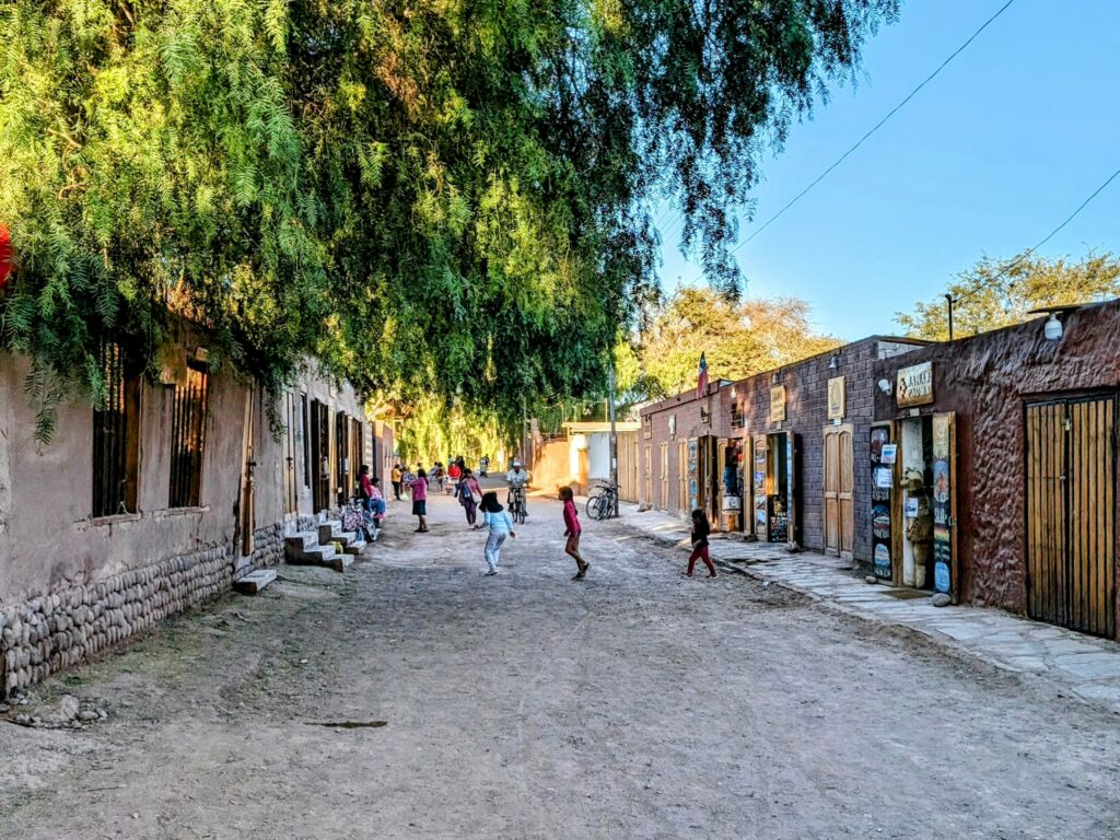 A pedestrian dirt street filled with kids playing and lined with clay retail buildings