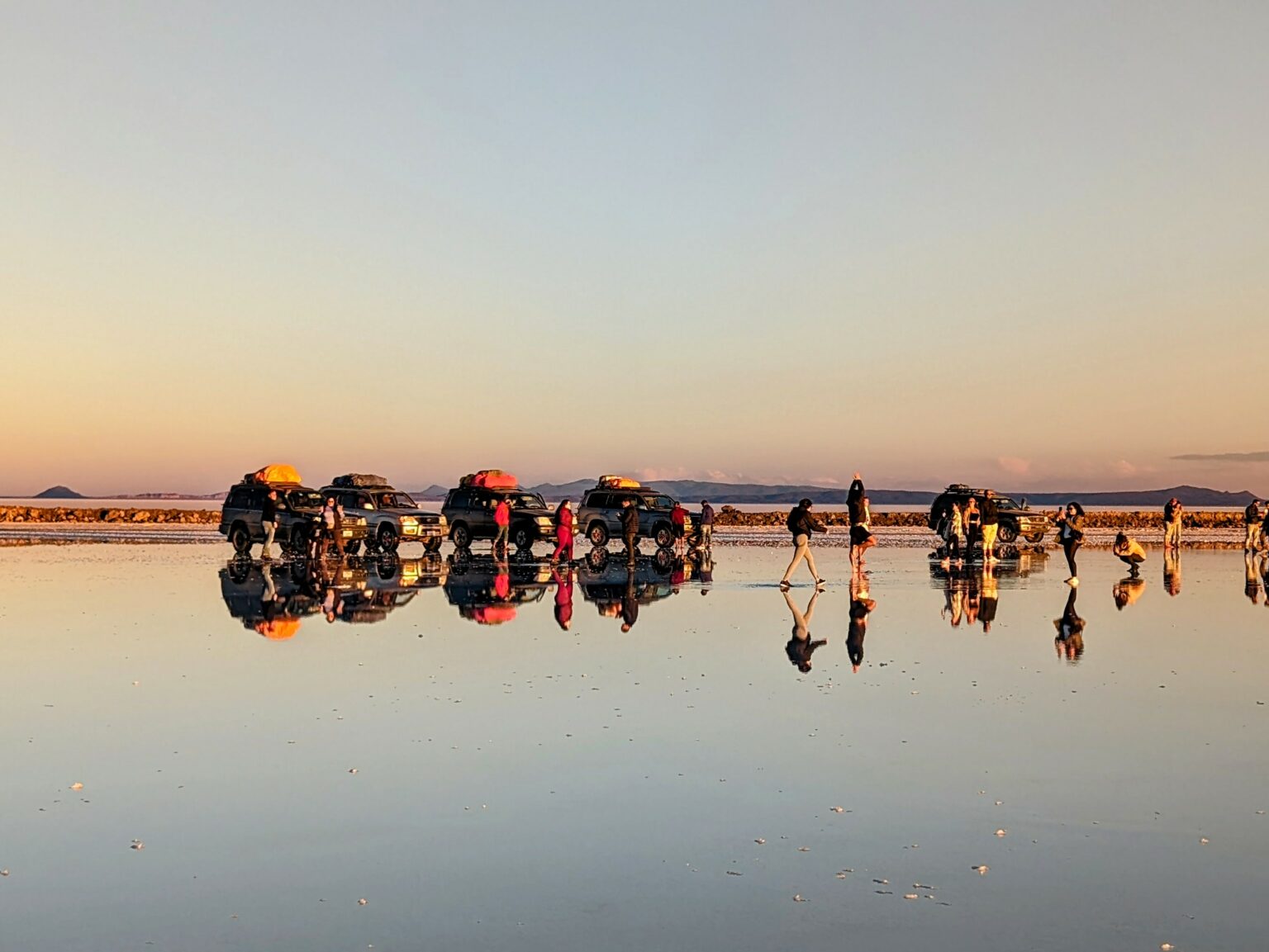Cars and people standing on a salt flat with a reflection during the Uyuni Salt Flats tour