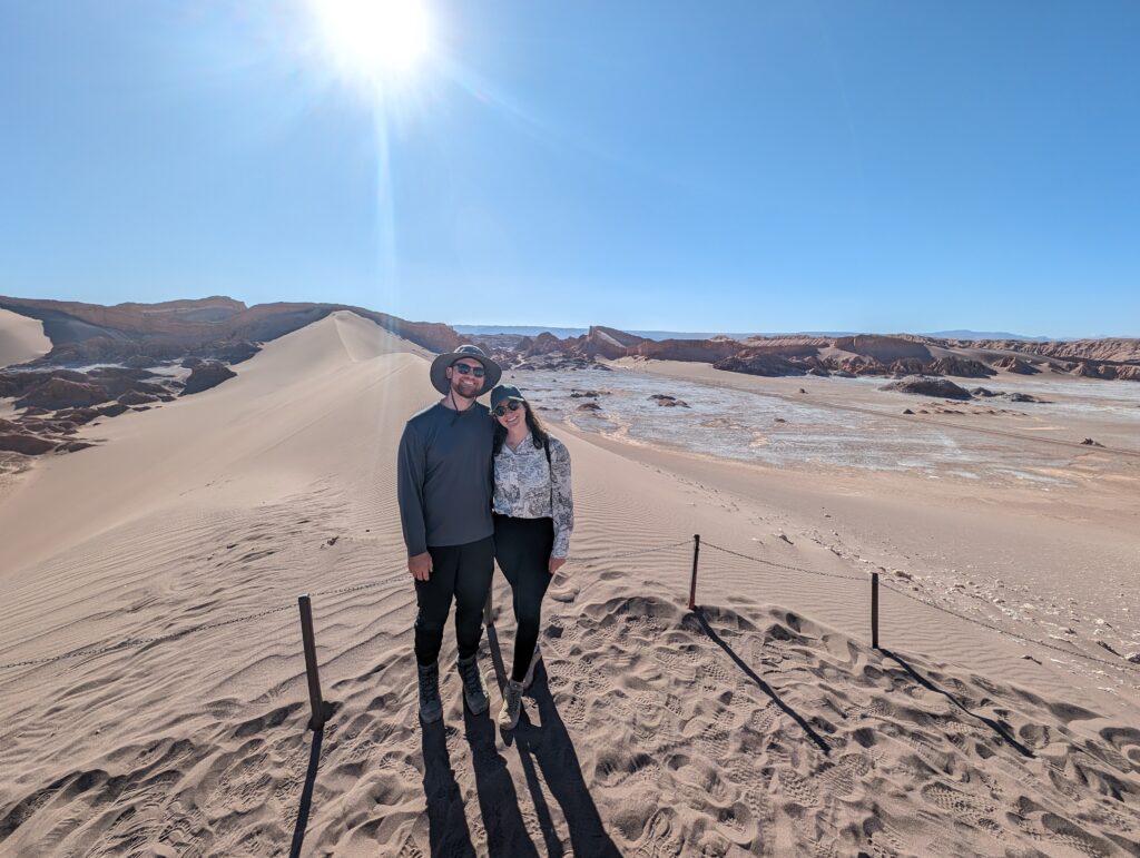 Two people standing in front of sand dunes in the Atacama desert