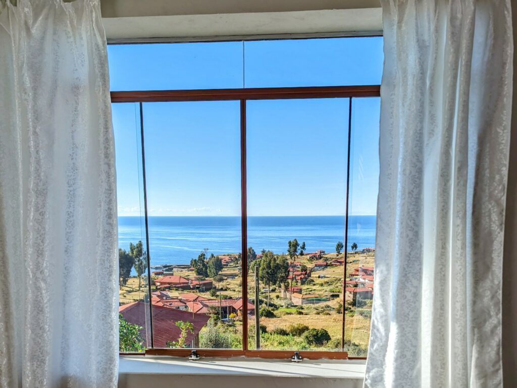 The view of a lake and greenery from a window as seen during the Lake Titicaca homestay tour