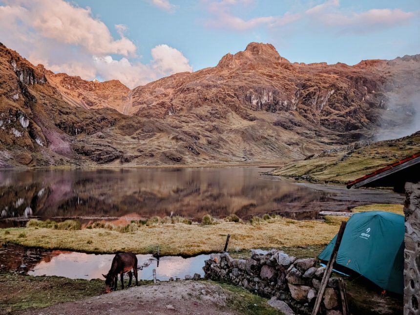 A tent in front of a lake with mountains in the background during a pink sunset on the Lares Trek - the landscapes are more beautiful when comparing the Lares trek vs Inca trail