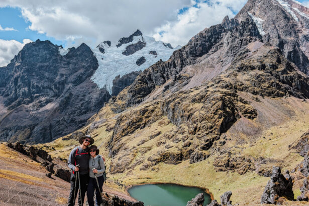 Two people standing in front of a turquoise lagoon in front of a snow-capped mountain