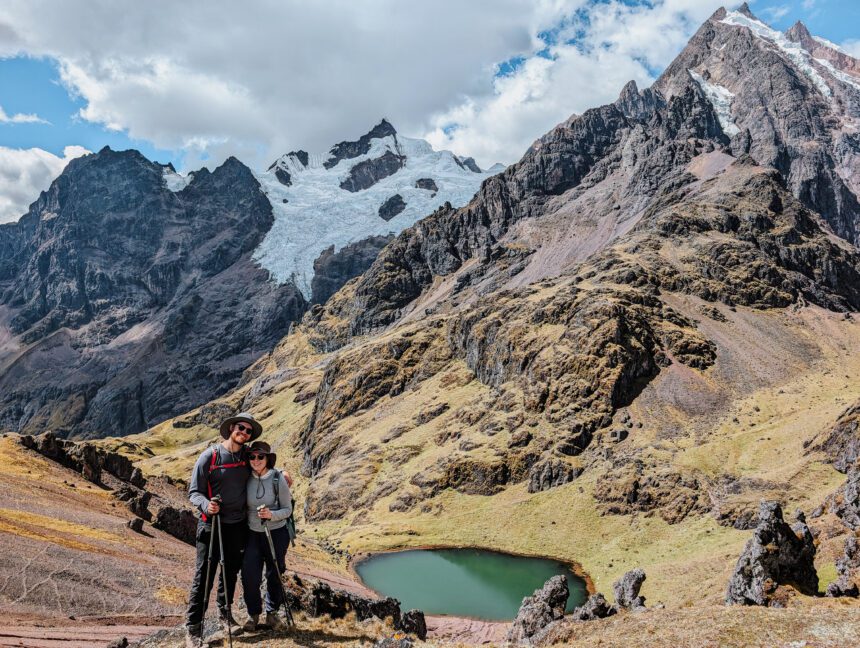 Two people standing in front of a turquoise lagoon in front of a snow-capped mountain on the Lares Trek Peru