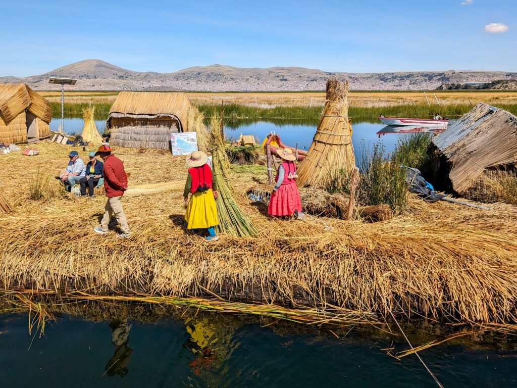 Three people in colorful clothing on an island made of reeds on a Lake Titicaca homestay tour