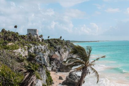 A white archaeological site in Mexico on the cliff of a tropical area with a white beach and turquoise water below