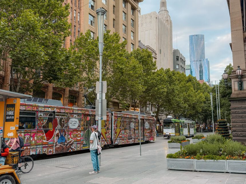 A tram car with art work on it going through the city - Melbourne city itinerary