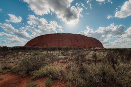 A large red rock under a lightly cloudy blue sky - 3 day uluru tour