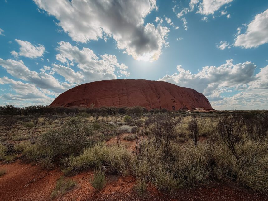 A large red rock under a lightly cloudy blue sky - 3 day uluru tour