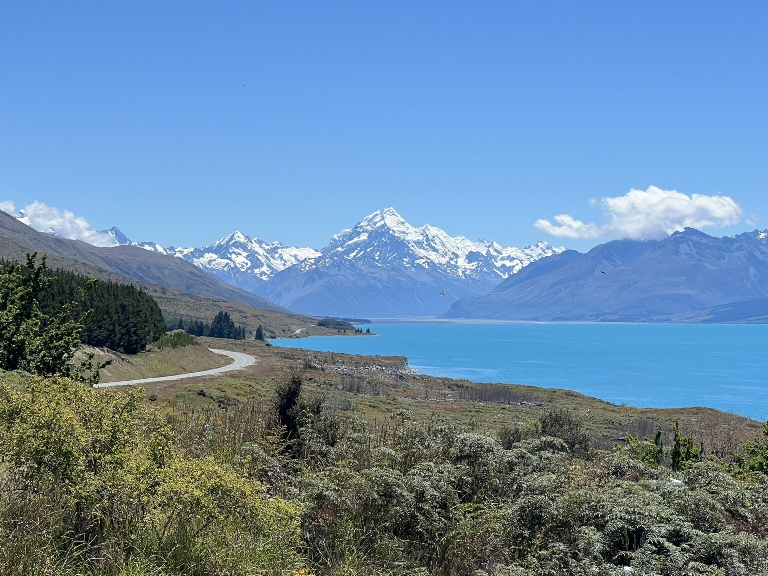 A teal blue lake beneath white-capped mountains on a trip from Christchurch to Dunedin