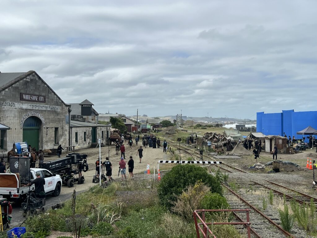 Trucks and people huddled in front of colonial style building in a town on a trip from Christchurch to Dunedin