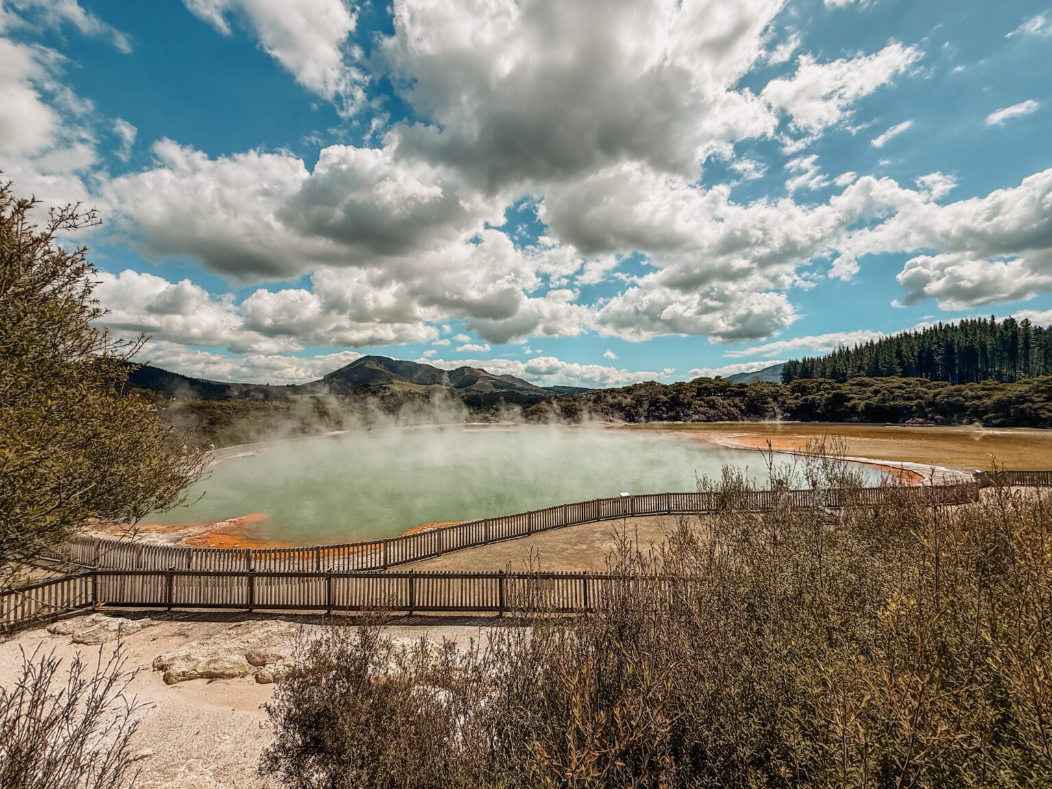 A turquoise and orange pond with steam rising from it in Rotorua