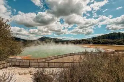 A turquoise and orange pond with steam rising from it in a Rotorua itinerary