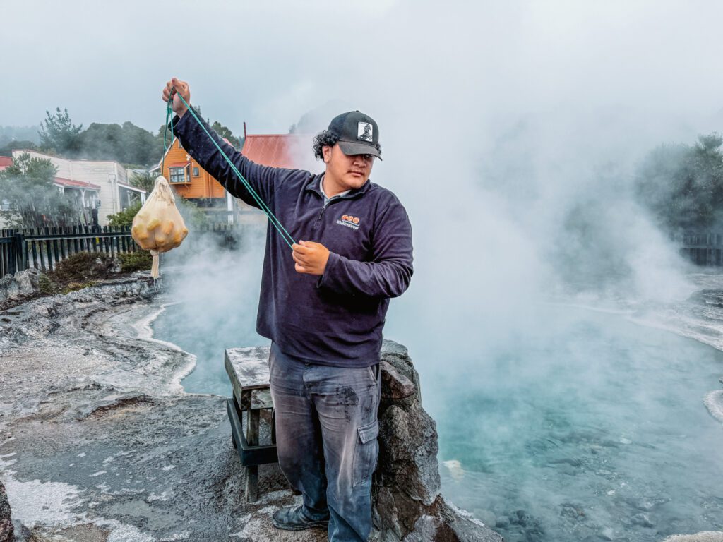 A man holding a bag of corn in front of a steaming pool in Rotorua