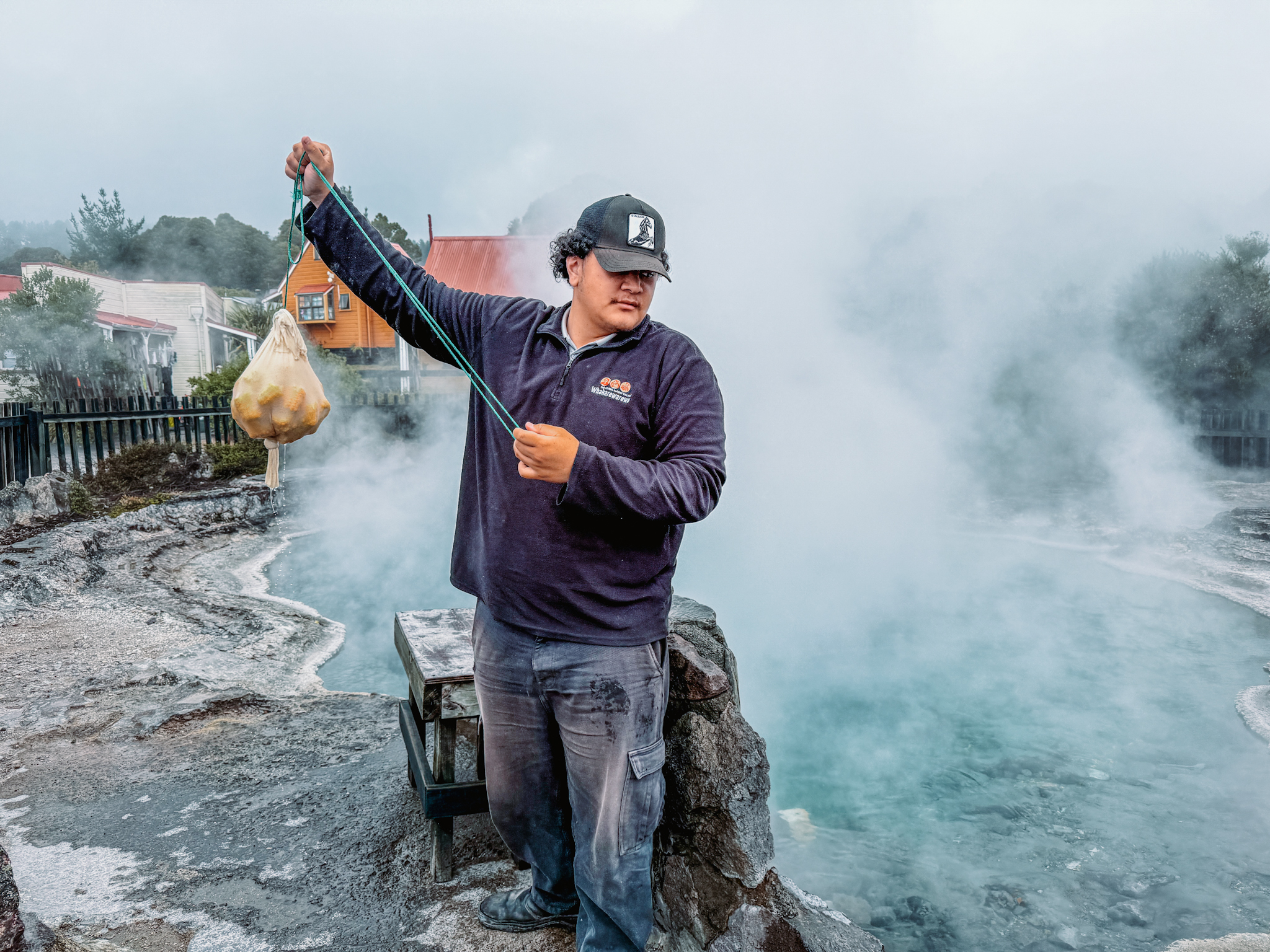 A man holding a bag of corn in front of a steaming pool as part of a Rotorua itinerary
