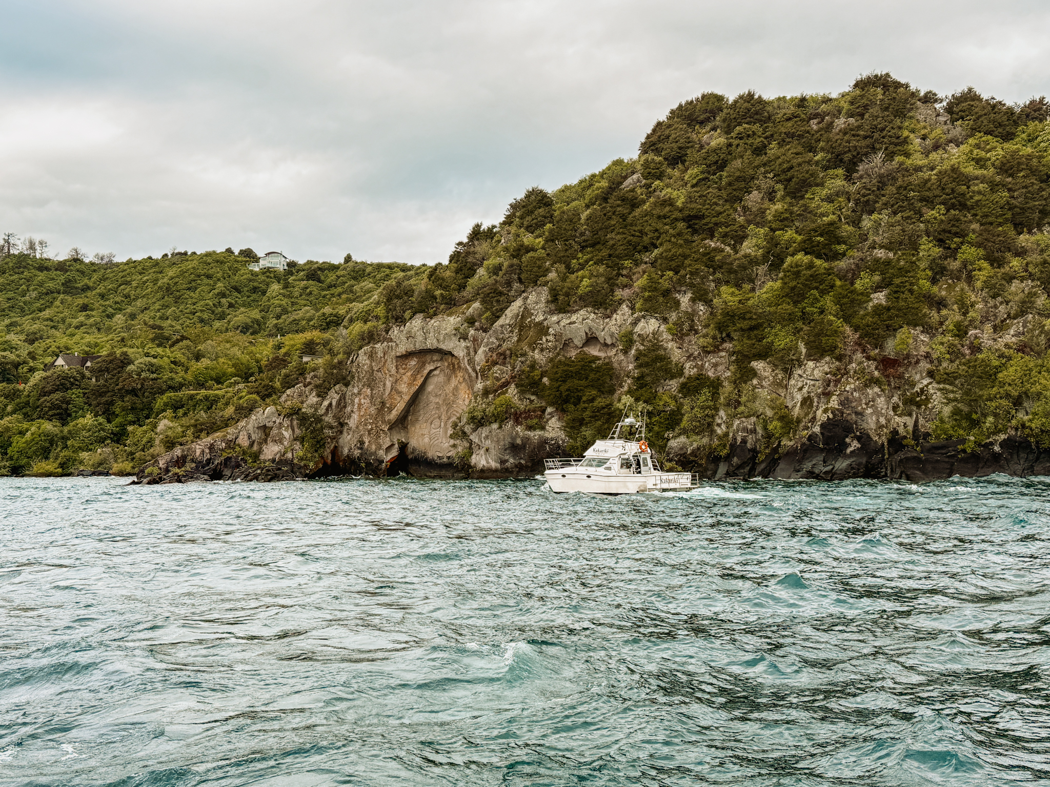 a boat on a lake against a rock cliff shore - activities Taupo has to offer